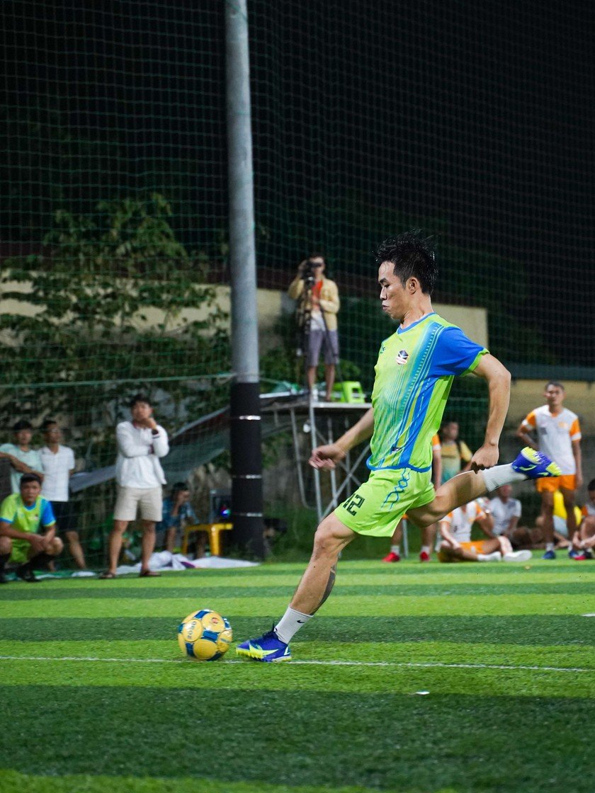 Footballer in a neon green and blue custom team kit striking the ball under floodlights at night