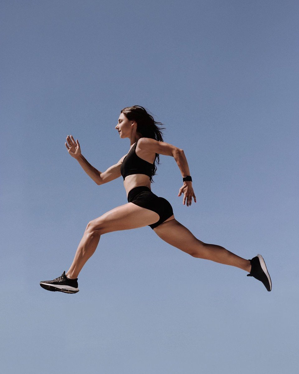 Athlete leaping mid-air against a blue sky in black training wear