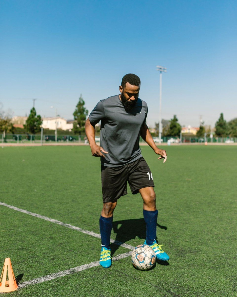Footballer dribbling on a sunny training pitch in a full kit