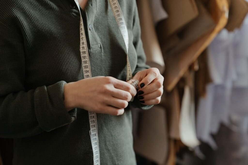 Tailor with measuring tape beside fabric rolls in a garment workshop